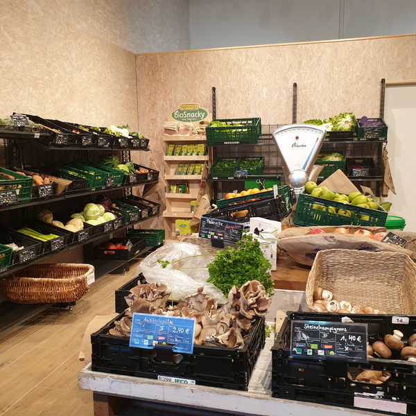 KI generiert: Ein Bio-Laden mit Obst, Gemüse und Pilzen. Text: Austerpilz 2,40 €/100g, BioSnacky, Steinchampignons 1,40 €/100g.