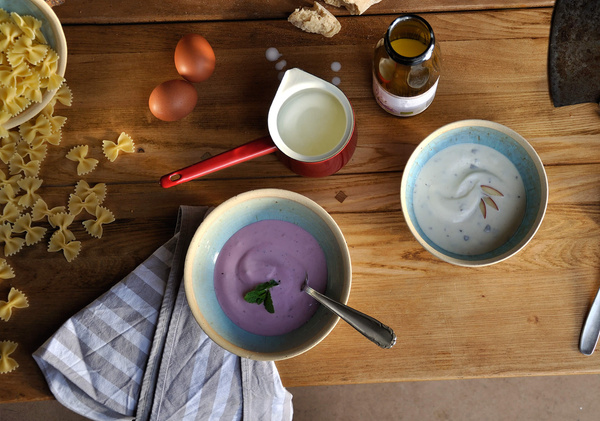 KI generiert: Verschiedene Zutaten auf einem Holztisch: Nudeln, Eier, zwei Saucen in Schüsseln, ein Krug und eine Flasche.