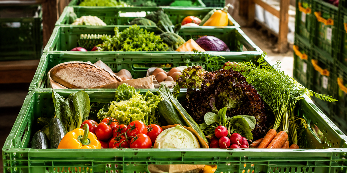 KI generiert: Kisten mit frischem Gemüse, Obst, Broten und Eiern aufgereiht in einer Reihe.