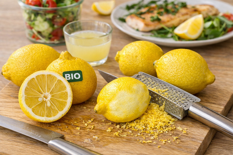 Bio-Zitronen auf Holzbrett mit Zitronenreibe, frischem Zitronenabrieb und Zitronensaft.