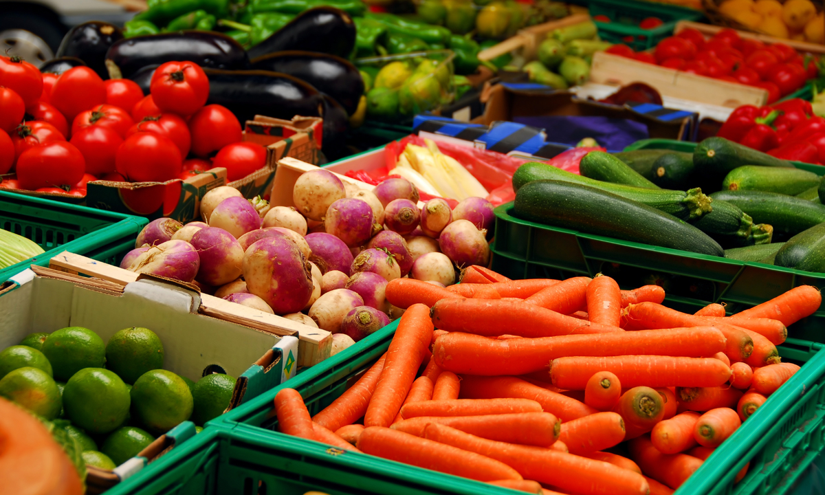 KI generiert: Frisches Gemüse auf einem Marktstand: Karotten, Tomaten, Zucchini, Auberginen, Limetten, rote Paprika.