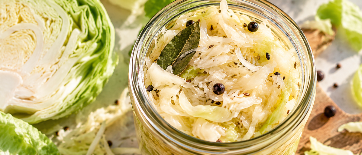 Fermentierter Weißkohl im Glas mit frischem Weißkohl und Gewürzen.
