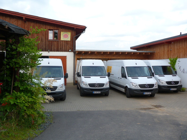 KI generiert: Vier weiße Lieferwagen parken vor einem Holzgebäude.