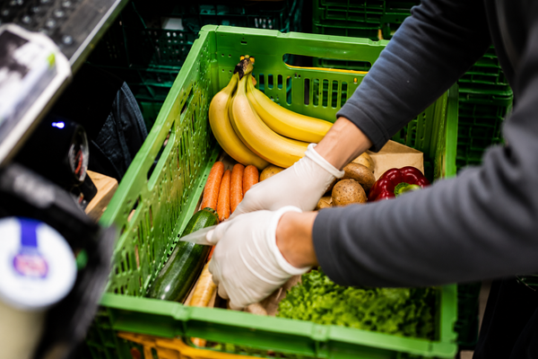 KI generiert: Eine Person sortiert frisches Obst und Gemüse in einer grünen Kiste.