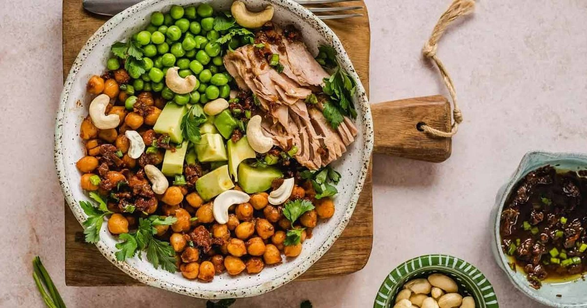 KI generiert: Eine bunte Schale mit Erbsen, Kichererbsen, Avocado, Nüssen und Fleisch auf Holzbrett.