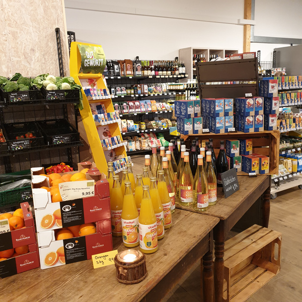 KI generiert: Ein Bio-Laden mit Obst, Tees und Säften. Text: "Glühwein weiß 3,99€", "Orange 3kg 9,95€".