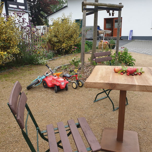 KI generiert: Garten mit Tisch, Stühlen und Kinderspielzeug. Auf dem Tisch liegen Obst und Zweige.