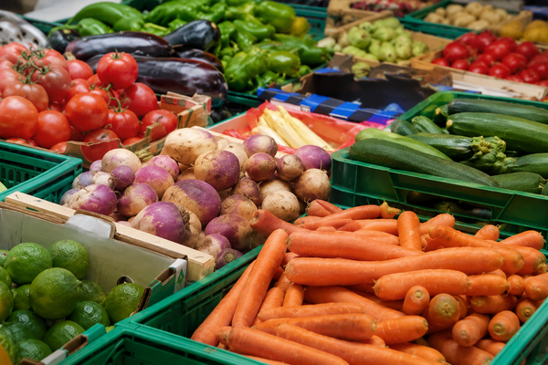 KI generiert: Frisches Gemüse auf dem Markt: Karotten, Tomaten, Zucchini, Auberginen, Limetten und mehr in Kisten.
