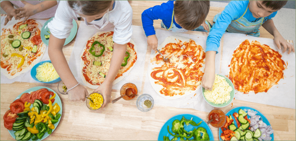 KI generiert: Kinder bereiten Pizzen mit Gemüsezutaten zu.