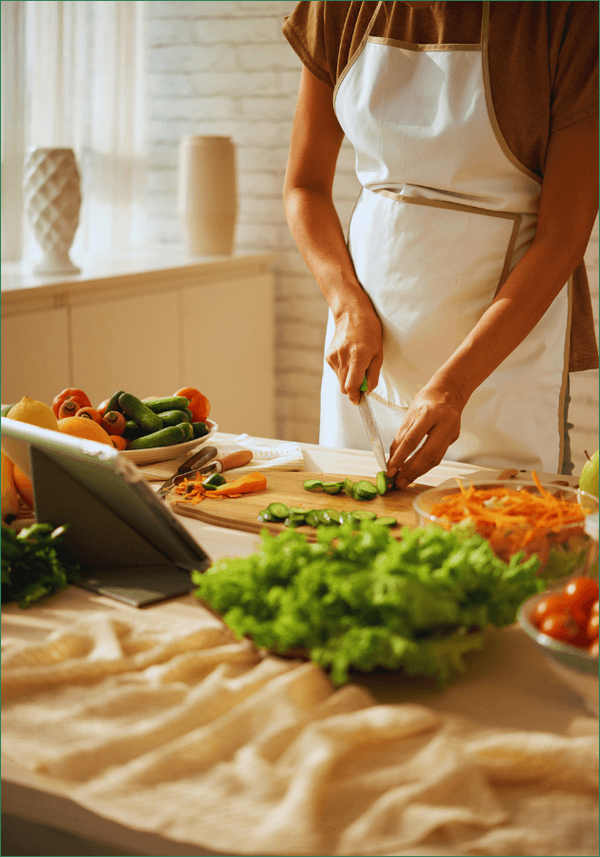 KI generiert: Person schneidet Gemüse in einer Küche. Vor ihr sind Salat, Möhren und Gurken. Ein Tablet steht auf dem Tisch.