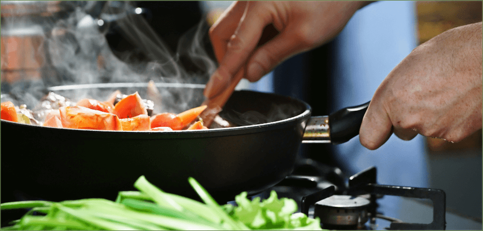 KI generiert: Eine Person kocht Karotten in einer Pfanne auf einem Herd, daneben liegen grüne Kräuter.