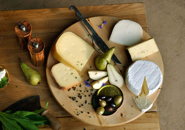 KI generiert: Käseplatte mit verschiedenen Käsesorten, Birnen, Oliven und einem Messer auf einem Holztisch.