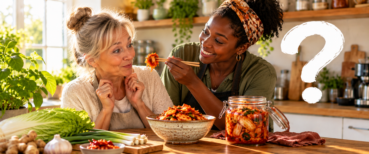 DuFrau bietet einer älteren Frau in einer hellen Küche Kimchi mit Essstäbchen an. Beide lächeln, während ein großes weißes Fragezeichen die Frage aufgreift, wie gesund Kimchi wirklich ist.