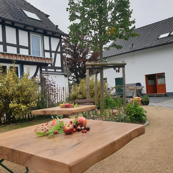 KI generiert: Ein rustikaler Garten mit Holztischen und verstreutem Obst vor Fachwerkhäusern.