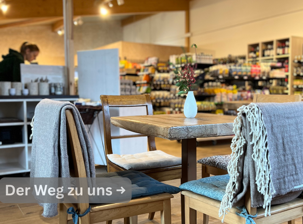 KI generiert: Ein gemütliches Café mit Tisch im Vordergrund. Text: "Der Weg zu uns →".