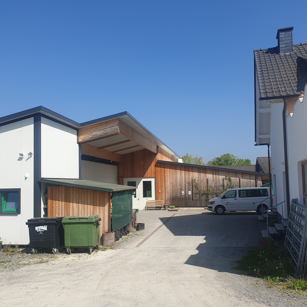 KI generiert: Moderne Gebäude mit Holzverkleidung, Mülltonnen und Lieferwagen; klarer, sonniger Himmel.