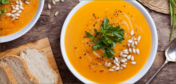 KI generiert: Eine Schüssel Kürbissuppe mit Petersilie und Kürbiskernen, daneben Brotscheiben.
