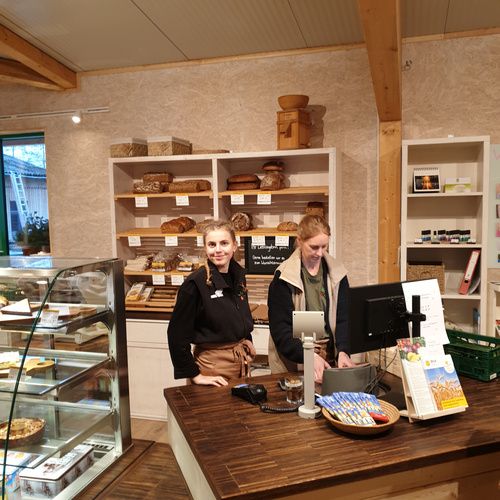 KI generiert: Zwei Personen stehen hinter einer Kasse in einem Bäckereiladen mit Brotregalen im Hintergrund.