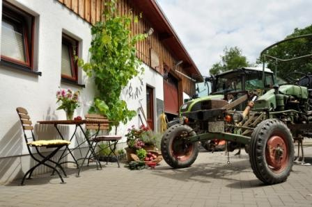 KI generiert: Ein Traktor steht vor einem ländlichen Gebäude, mit Tisch und Stühlen daneben.