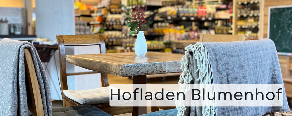 KI generiert: Ein gemütlicher Tisch im Hofladen mit Decken. Text: "Hofladen Blumenhof".