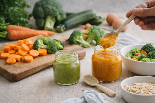 KI generiert: Hausgemachter Babybrei in Gläsern mit frischem Gemüse und Haferflocken auf einem Tisch arrangiert.